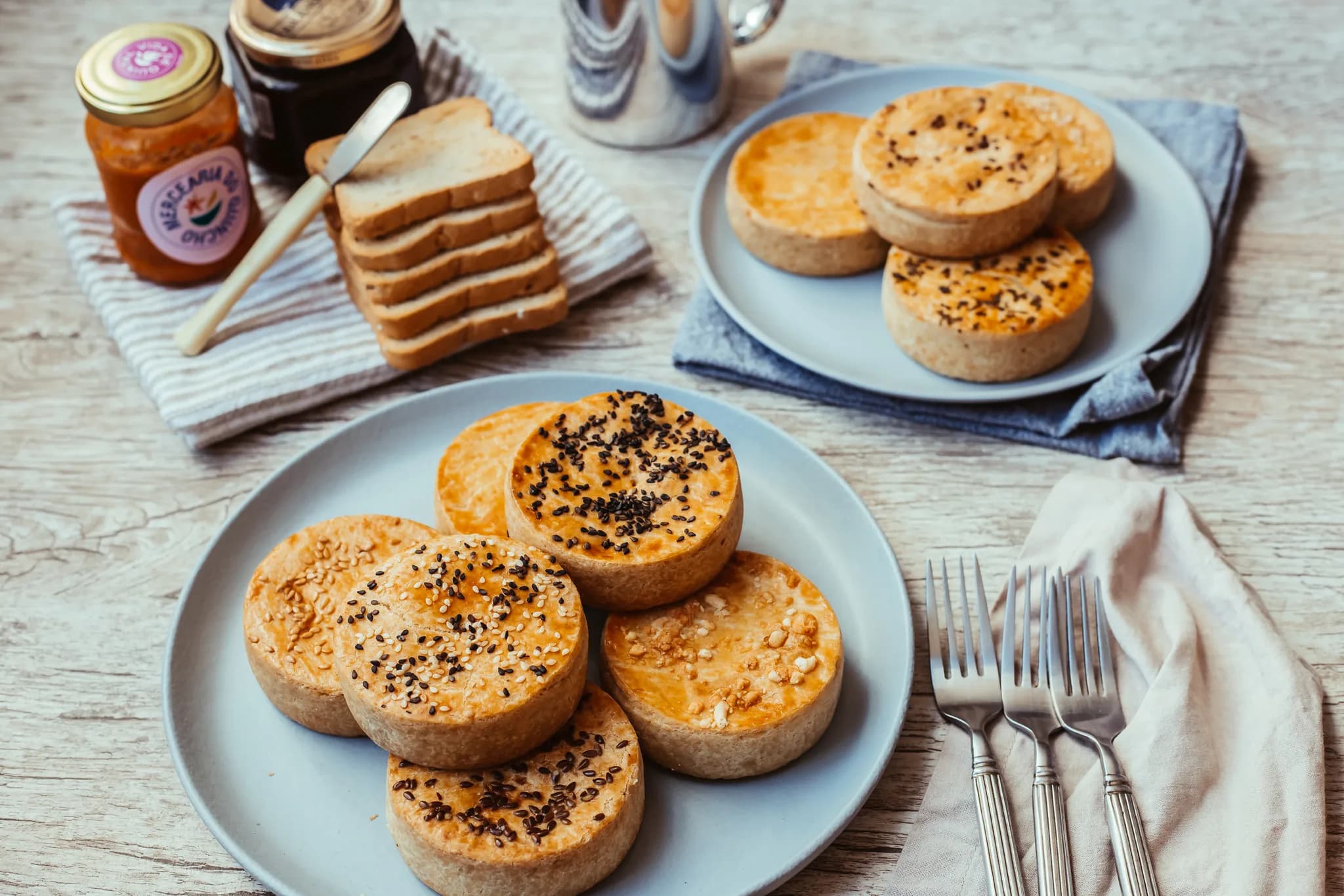 Mesa posta com mini tortas e quiches variadas em dois pratos, pães, geleias e café